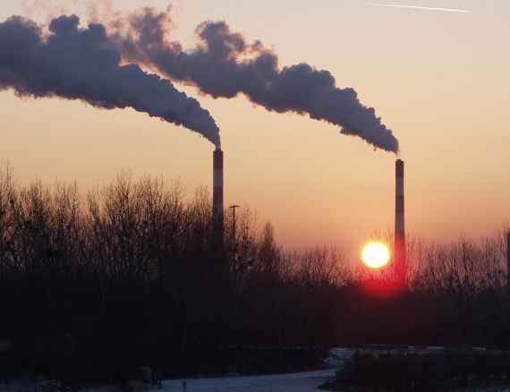 Industrieschornsteine mit Rauchfahnen bei Sonnenuntergang.